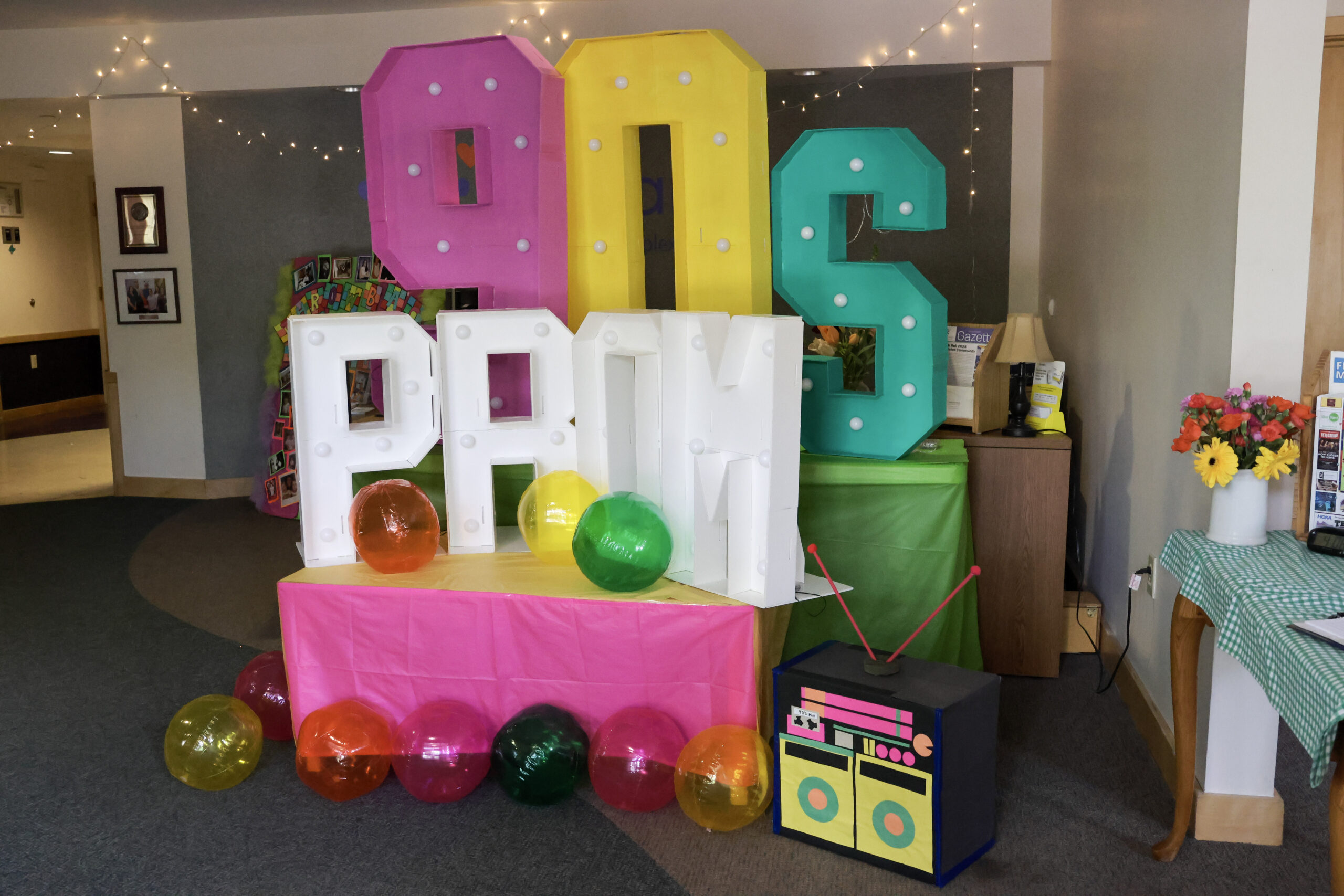 Colorful 90s PROM display with balloons, a boom box, and string lights, evoking a retro party vibe.